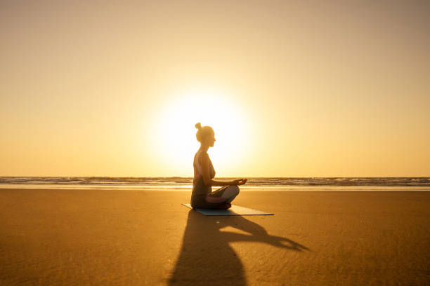 Silhouette of young woman in a stylish suit for yogi jumpsuit doing yoga on the beach in pose copy space stock photo