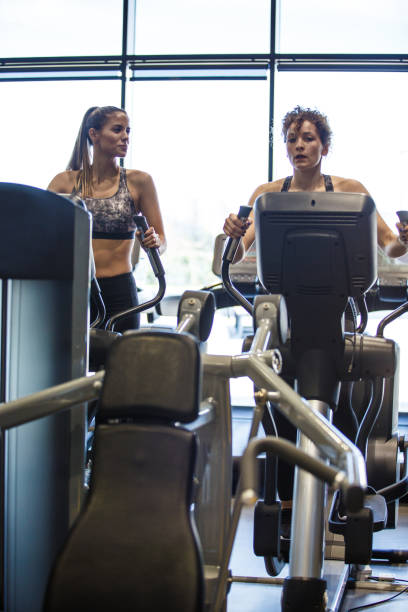 istock Two athletic female friends having a conversation while warming up on elliptical machines 1419445565