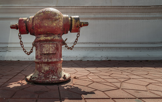 Bangkok, Thailand - Apr 15, 2022 : A Old red fire hydrant on sidewalk in Front of an on white cement wall for fire fighting on land, the water is pumped through the hydrant to a tank on a fire. Copy space, Selective focus.