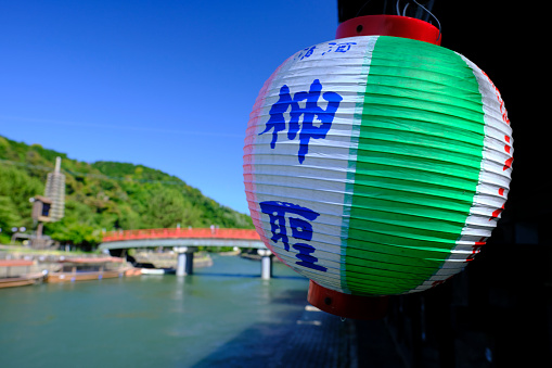Uji, Japan - June 12, 2022: A paper lantern hangs next to the scenic Uji River, where fishermen use cormorants to catch fish at night. There are several cafes and restaurants catering to tourists along the river. Byodoin Temple, which appears on Japan's 10-yen coin, is a short walk away.