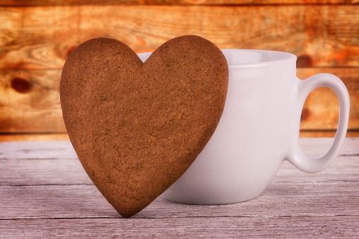 Heart shaped hand made cookie and white coffee mug on wooden plank in background. Valentines day concept.