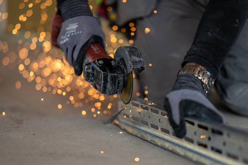 Electric saw and sparkles close view. Metalwork concept. Workman in protective gloves cutting metal plank with angle grinder