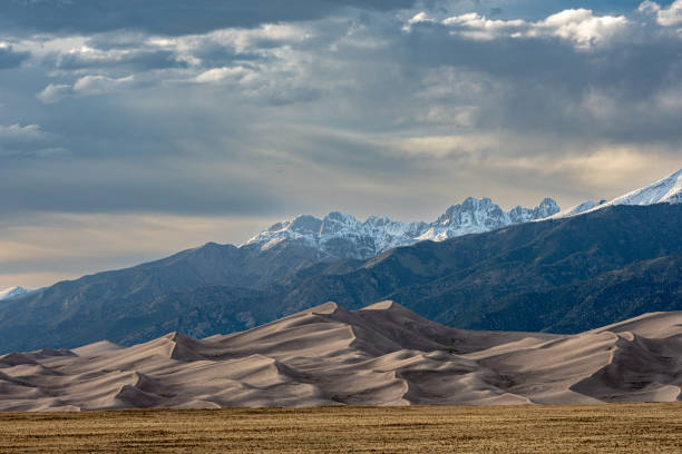 Wind Swept Dunes Below Snow capped Mountains Wind Swept Dunes Below Snow capped Mountains in Colorado park great sand dunes national park stock pictures, royalty-free photos & images