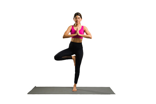 Full length of a happy relaxed young woman exercising and doing a tree yoga pose against a white background