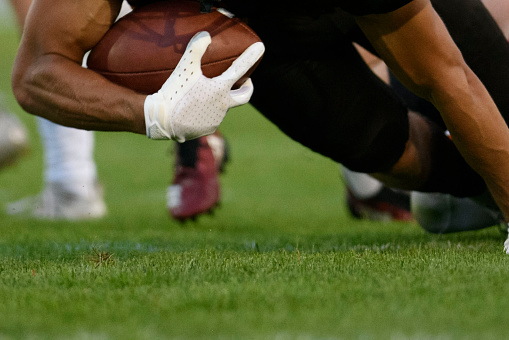 A football player scores a touchdown and falls to the grass