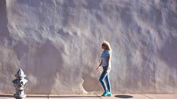 istock Woman Walks by Sunlit Adobe Wall, Fire Hydrant, Southwest USA 1419464515
