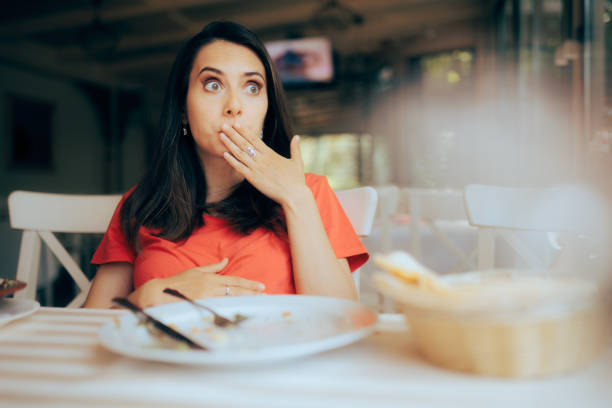 mujer divertida que se siente llena después de comer una gran porción de comida - comer demasiado fotografías e imágenes de stock