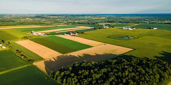 A view of rural wisconsin landscape with farms and fields. Trees surround the area with a blue sky above.