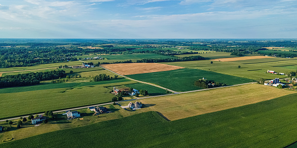 A view of rural wisconsin landscape with farms and fields. Trees surround the area with a blue sky above.