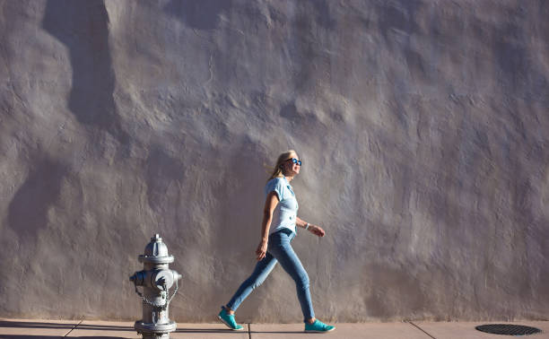 istock Woman Walks by Sunlit Adobe Wall, Fire Hydrant, Southwest USA 1419472079