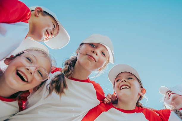 i bambini in età elementare sono atleti che giocano a baseball insieme in una squadra sportiva co-ed con allenatori al campo da gioco - baseball player sport little league looking up foto e immagini stock