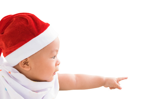 Happy little Asian baby boy in red santa claus hat celebrate christmas isolated on white background. The kid pointing his finger out in front of the new year holiday. Breastfeeding childhood development.