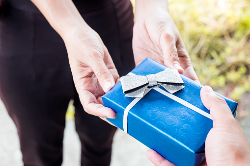 Close up of hand boyfriend giving present package his girlfriend Anniversary birthday. Surprising blue gift box wrapped in ribbon bow. Merry Christmas. Happy new year. Valentine's day.