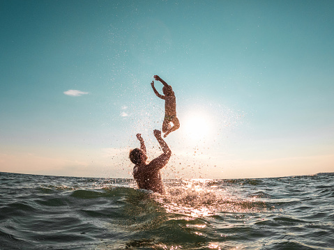 Happy boy enjoying a careless childhood at the sea. He is jumping, playing, laughing and having fun with his dad. They are in the water together.