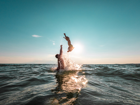 Young multi ethnic guys jumping off a jetty into a lake in Derwent Water in Cumbria