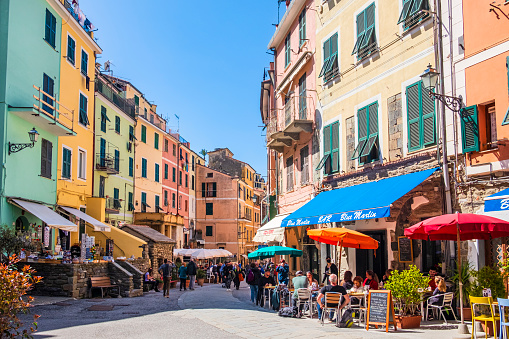 Tourists strolling in via Roma in Vernazza, bordered by pastel colored buildings with restaurants and bars