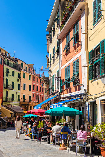 Tourists sitting at the outdoor tables in via Roma in Vernazza, bordered by pastel colored buildings
