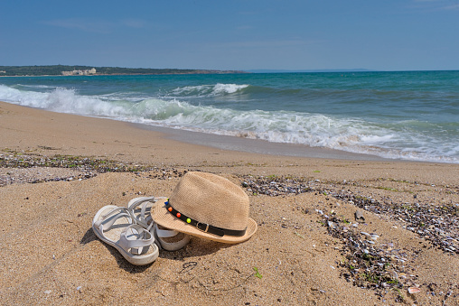 White summer sandals and a straw hat on a sandy beach in the background the sea and the beach
