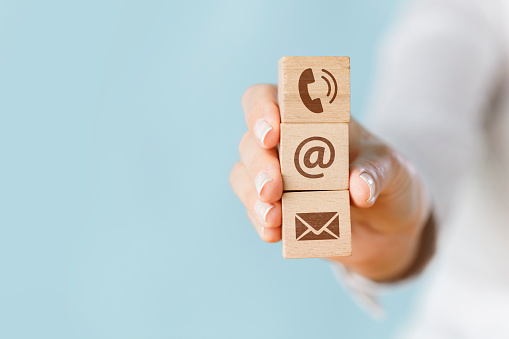 Female hand holding wooden block cube symbol telephone, envelope email and address sign. Website page contact us or social media concept