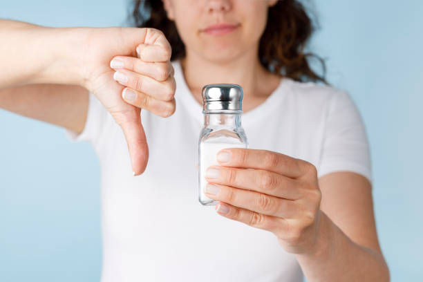 Young woman with salt shaker, negative sign showing dislike for foods that are too salty stock photo