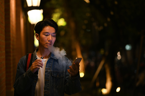 Young hipster man using mobile phone while walking through the night city streets. Night life concept.
