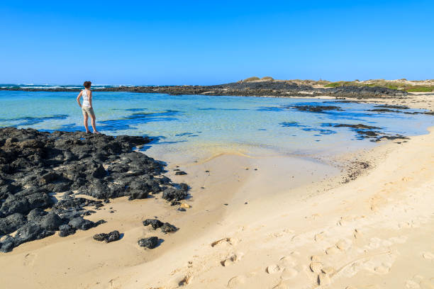 young woman standing on rock in beach lagoon in el cotillo town, fuerteventura, canary islands, spain - el cotillo imagens e fotografias de stock