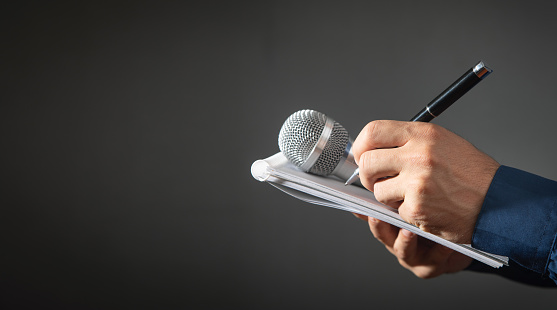 Caucasian journalist holding microphone, notepad and pen.