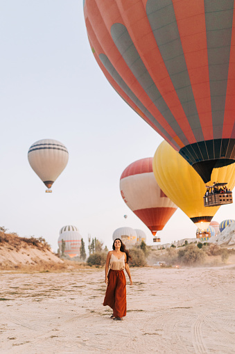 Young woman is walking and smiling near hot air balloons in Cappadocia