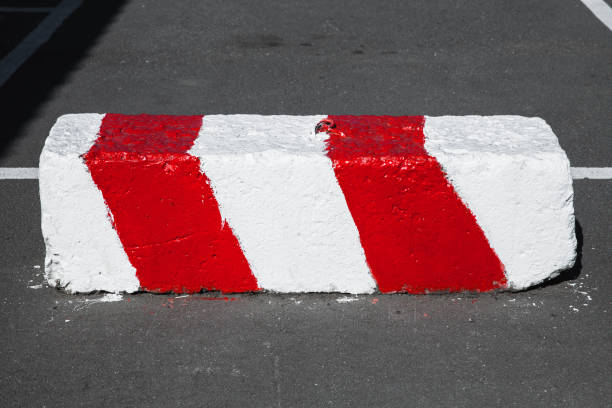 Road block made of concrete with warning red white diagonal striped pattern lays on an urban road