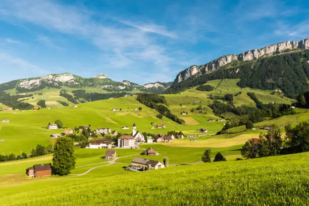 The village of Schwende in idyllic mountain landscape against blue sky with green meadows and pastures, Appenzellerland, Canton Appenzell Innerrhoden, Switzerland