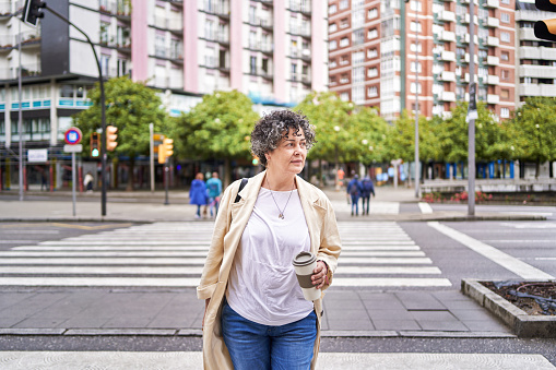 Front view of a mature woman looking sideways as she crosses the street at the crosswalk in the city.