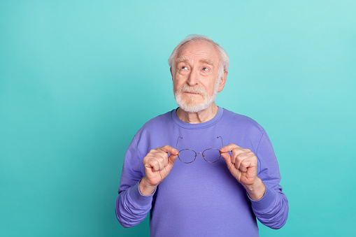 Portrait of focused minded granddad arms hold glasses look interested empty space isolated on teal color background.
