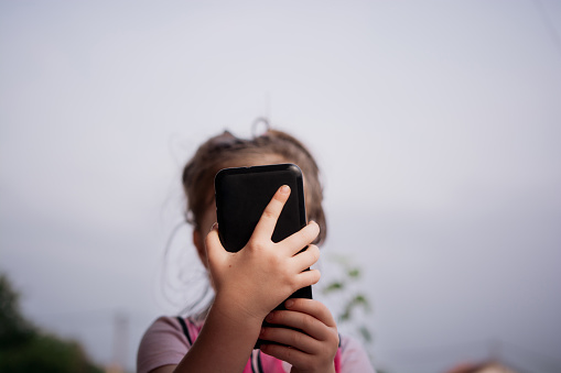 Close-up of unrecognizable girl holding mobile phone in front of her face outdoors
