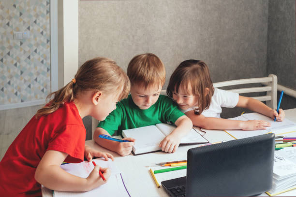 istock Children sit at a table with pens and notebooks and use a laptop 1419527416