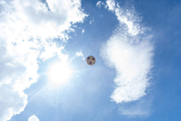 Classic black and white soccer ball football floating in bright blue summer sky