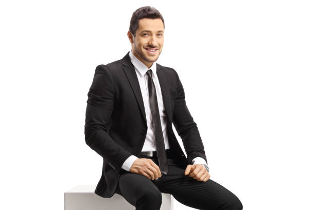istock Businessman sitting on a white cube and looking at camera 1419531807