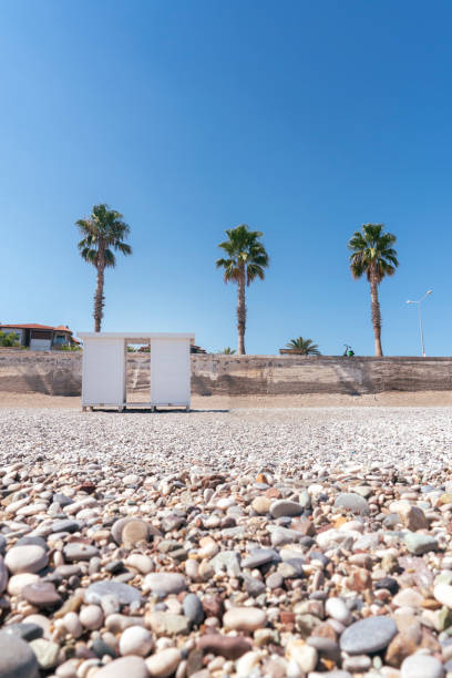The stones of Konyaaltı Beach, white changing cabins and palm trees lined along the coastal road