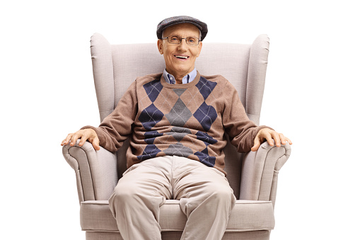Elderly man sitting in an armchair and smiling at the camera isolated on white background