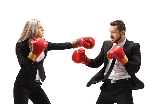 Young businesswoman hitting a businessman with boxing gloves isolated on white background