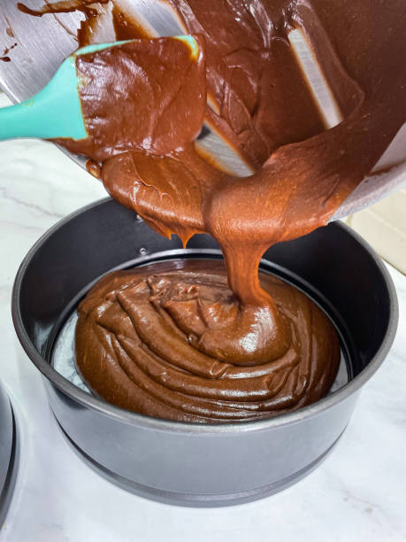 immagine di pastella di pan di spagna victoria al cioccolato fatta in casa, miscela di burro, zucchero, farina e cacao raschiata dalla ciotola di plastica, versando in una tortiera antiaderente rivestita con carta pergamena antigrasso, bancone da cucina ef - cake batter foto e immagini stock