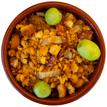 Typical dish of Castile and Leon cuisine - migas pastoriles from fried bread crumbs with diced chorizo and bacon served with grapes. Isolated over white background