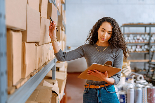 Logistics, delivery and ecommerce, warehouse worker checking stock in a warehouse. Businesswoman checking cargo for shipping in online shopping store. Woman working in inventory management industry.