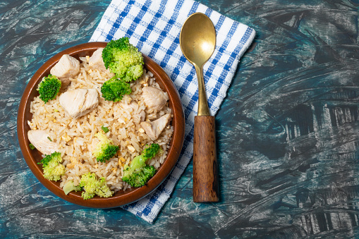 Fried rice dish with chicken breast have vegetable broccoli in bowl isolated on wood background close up, top view, healthy food and drink concept.
