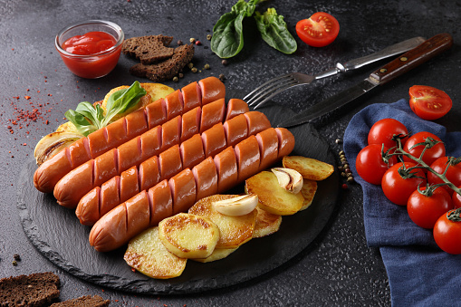 German cuisine. Hanover pork sausages fried on the grill with a potato on a black background. Nearby is ketchup. background image, copy space