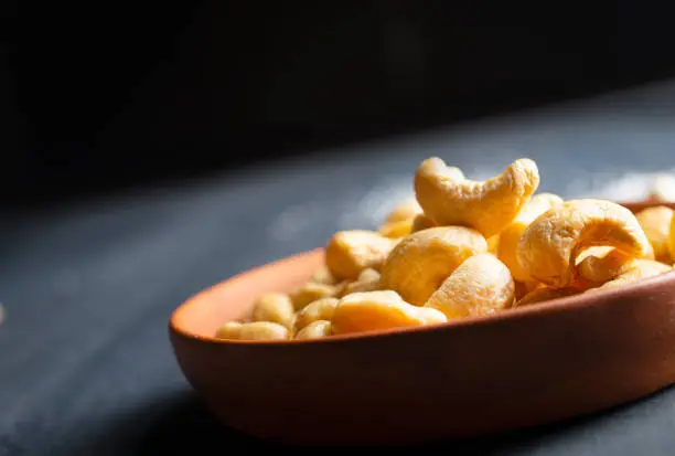 Tasty cashew nuts in bowl on dark table, top view