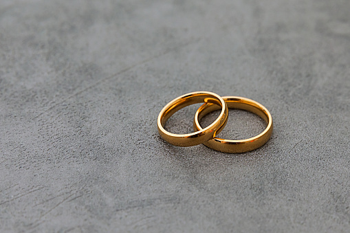 Pair of gold wedding ring bands jewelry in sand on tropical desert island beach during summer with blue ocean background