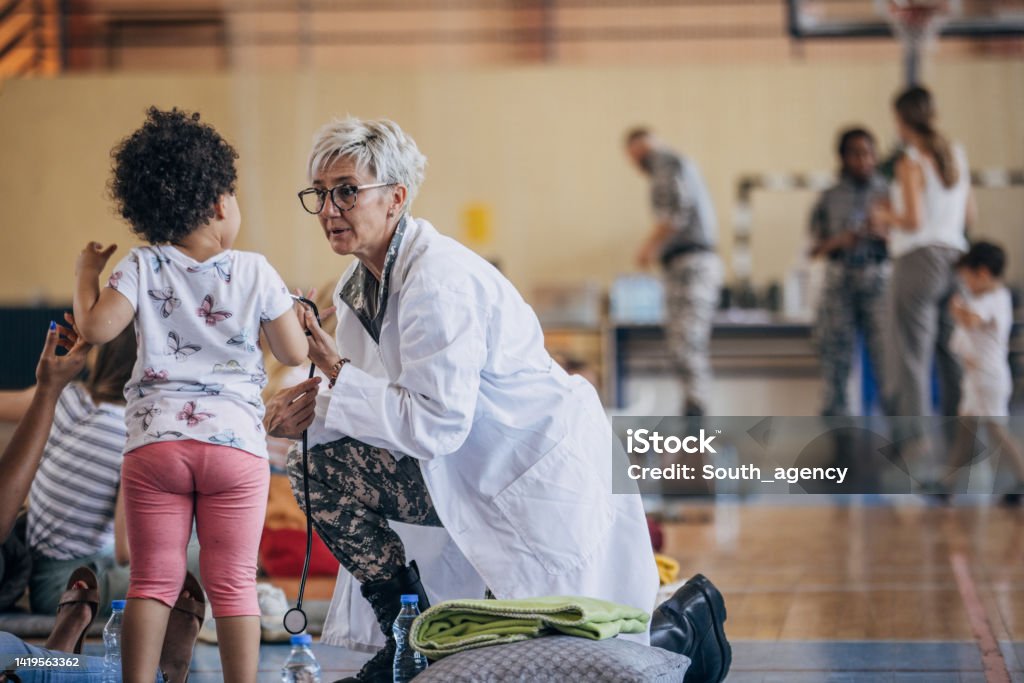 Army doctor with civilians after natural disaster Diverse group of people, soldiers on humanitarian aid to civilians in school gymnasium, after natural disaster happened in city. Refugee Stock Photo
