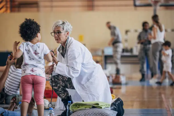 Diverse group of people, soldiers on humanitarian aid to civilians in school gymnasium, after natural disaster happened in city.