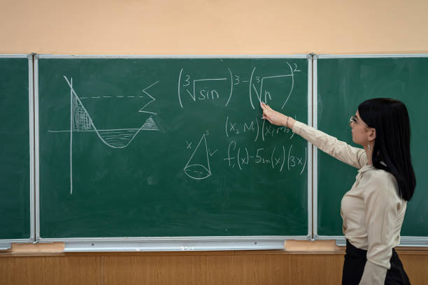 istock young pretty female teacher writing on a chalkboard completing mathematical equations in classroom 1419563501