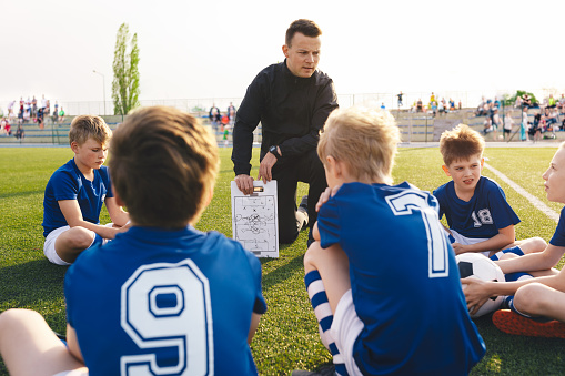 Coach explains a game strategy using board. Young coach teaching kids on football field. Football coach coaching children. Soccer football training session for children. Football tactic education